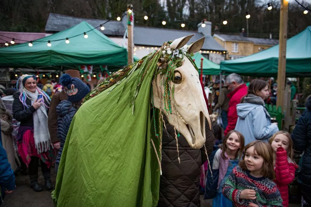 A horse with a green cape and a child in the background AI-generated content may be incorrect.